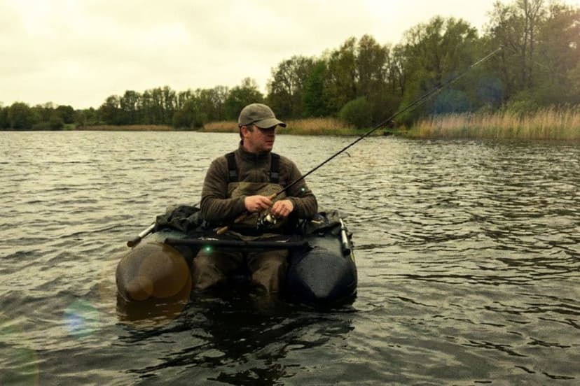 Angler im Belly Boot auf ruhigem See beim Spinnfischen