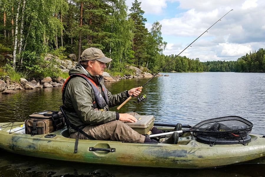 Angler im Sit-on-Top Kajak beim Hechtangeln auf ruhigem See mit Spinnrute